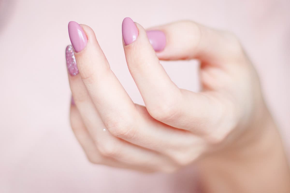 Close-up of a hand with glossy pink almond nails and one glitter accent nail against a soft pink background