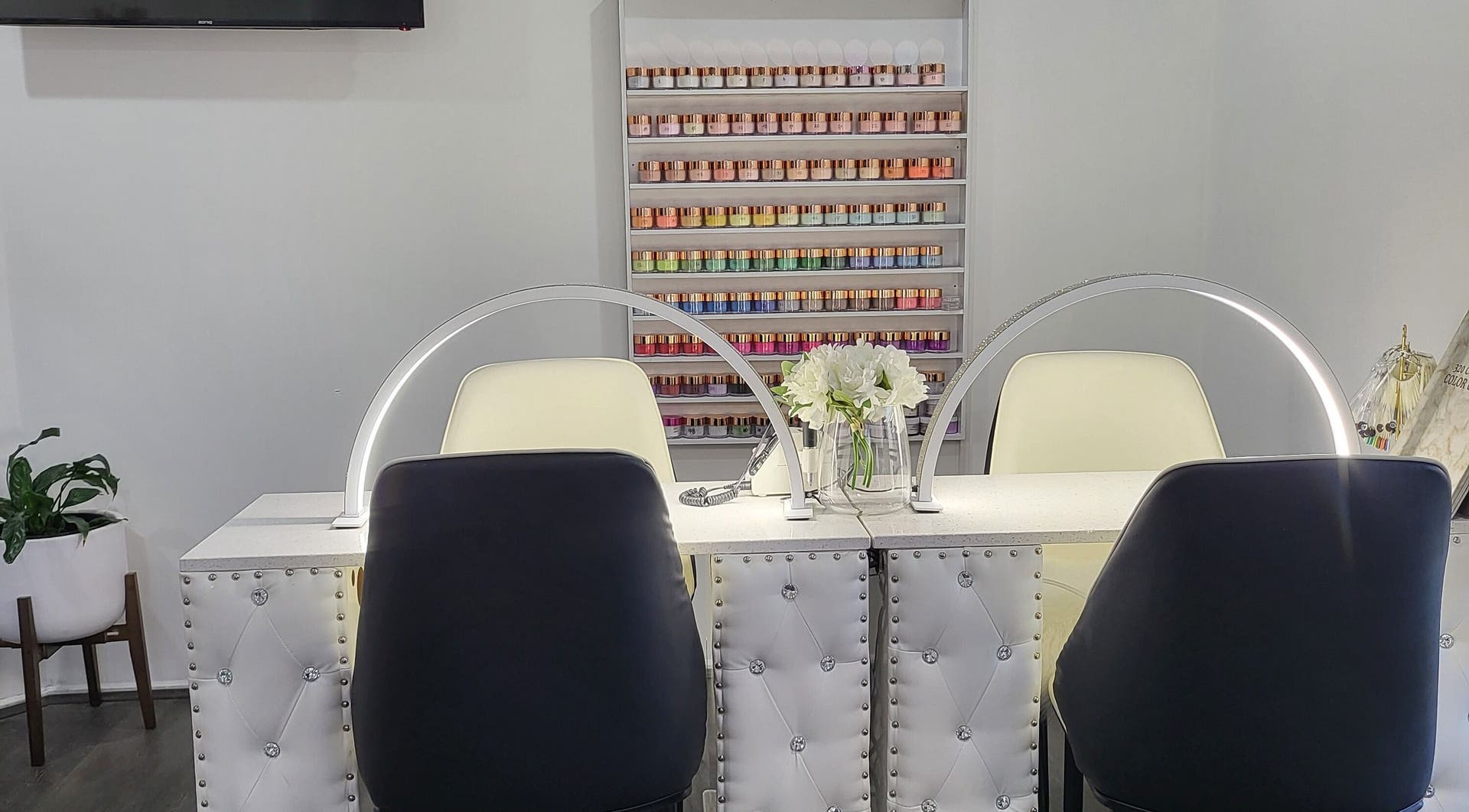 Two manicure stations with arc lamps, fresh flowers and a wall of colourful nail powders